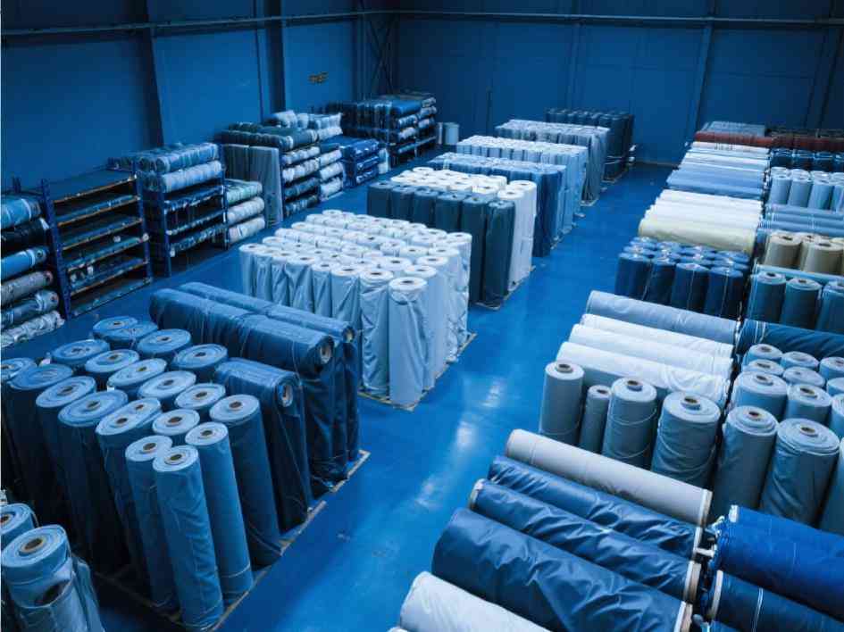 Warehouse interior with stacked PVC, PE, polyester, and Oxford fabrics – durable, waterproof, weather-resistant materials for industrial tarps, agricultural covers, outdoor tents & home protection products