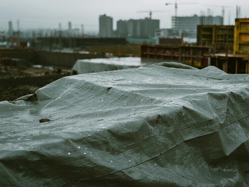 Workers securing tarp over gravel pile