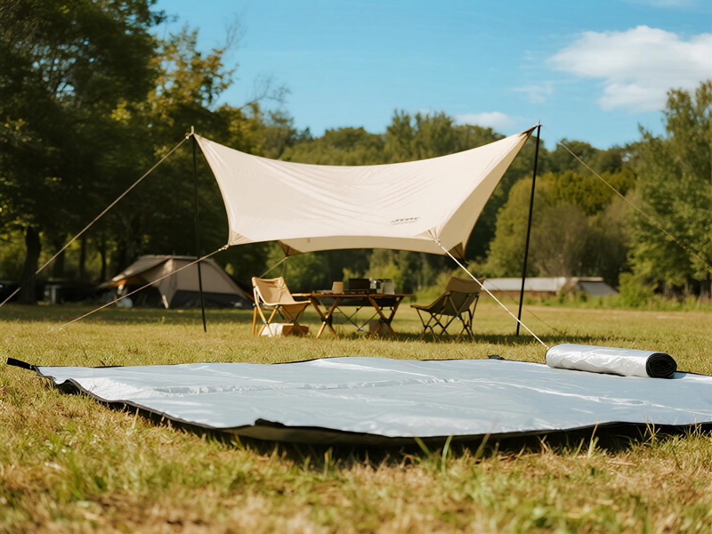 Polyester waterproof camping tarp laid under tent in forest setting